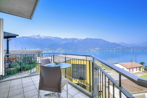 A balcony with a table and chairs, overlooking a lake and mountains. - Casa Zaira 2 3BR in Caviano Gambarogno (Gambarogno)