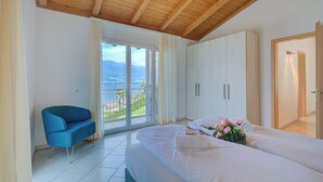 Ein Schlafzimmer mit einem großen Bett, einem blauen Sessel, einem Kleiderschrank und einem Balkon mit Meerblick.