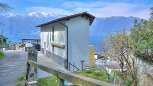 Ein kleines Gebäude mit weißer Fassade und braunem Dach, in der Nähe einer Straße mit Blick auf einen See und Berge im Hintergrund.