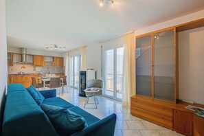 En moderne stue med sofa, spiseplads, køkken og en stor skydedør, der fører ud til en balkon.