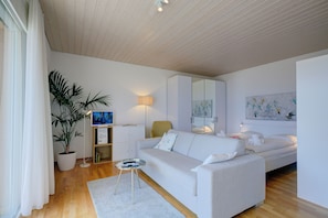 A modern living room with a sofa, a coffee table, a lamp, a plant, a bookshelf, and a bed. - Casa Miramonti Muralto (Muralto)