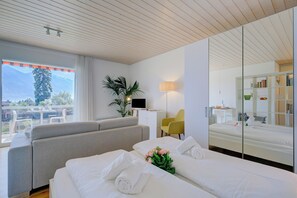 Een hotelkamer met een bed, een slaapbank, een bureau, een stoel, een televisie en een balkon met uitzicht op de bergen.