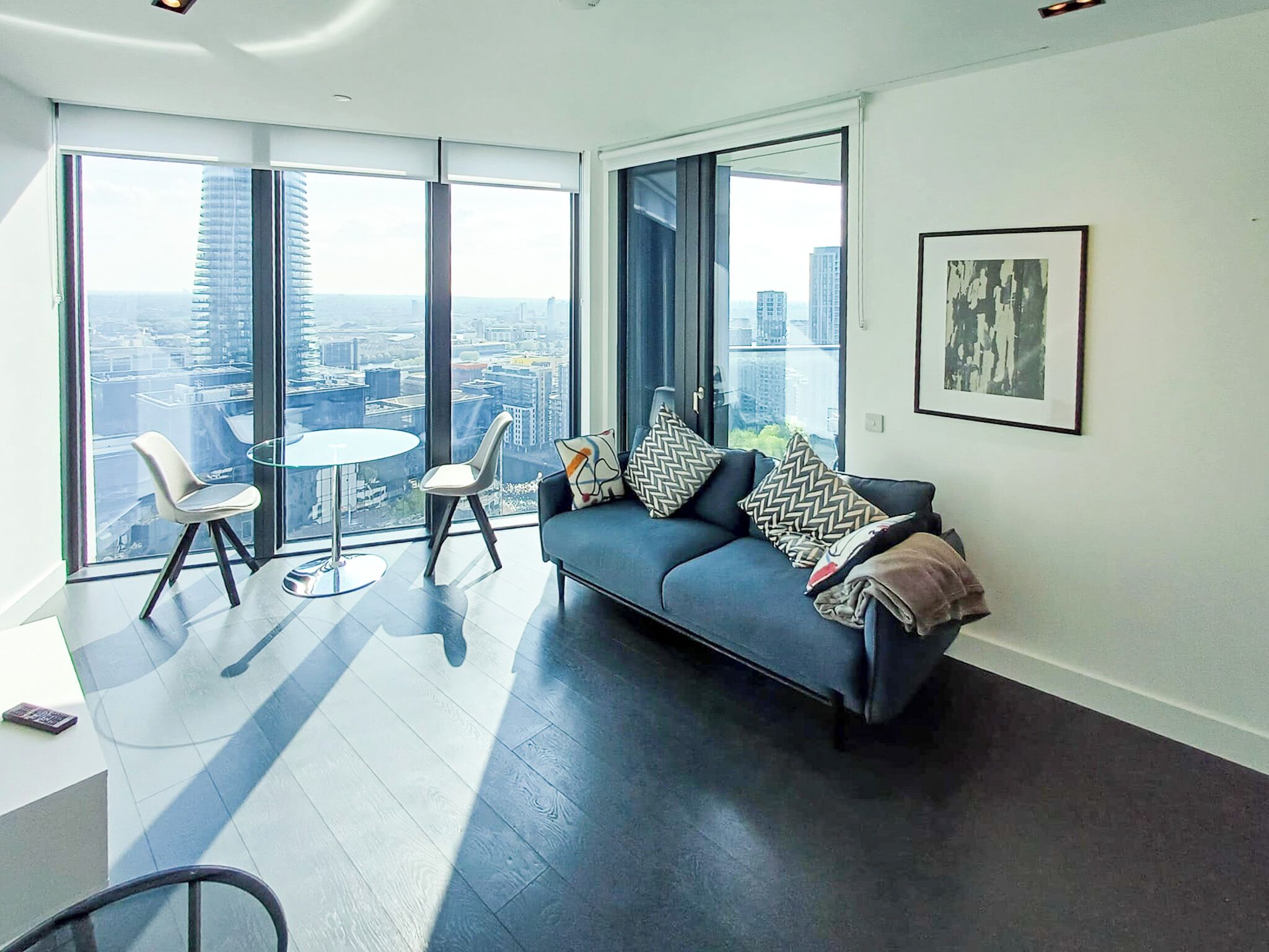 A modern living room with a sofa, two chairs, a small table, and large windows offering a city view.