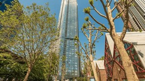 A modern high-rise building with a glass facade, surrounded by trees and other buildings. - One Bedroom Apartment City View (London)