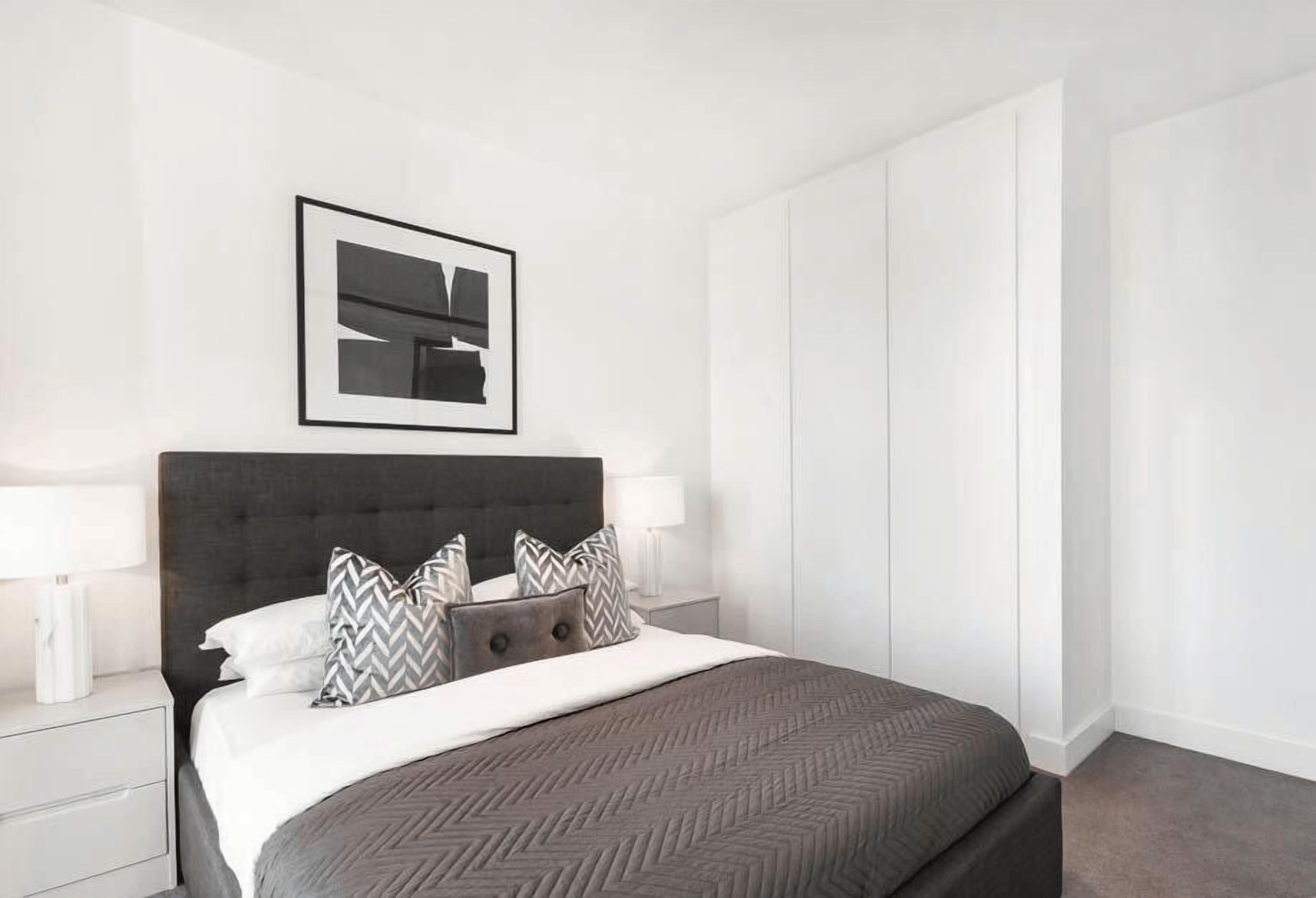 Une chambre à coucher moderne avec un grand lit, une tête de lit sombre et une œuvre d’art abstraite encadrée au-dessus.