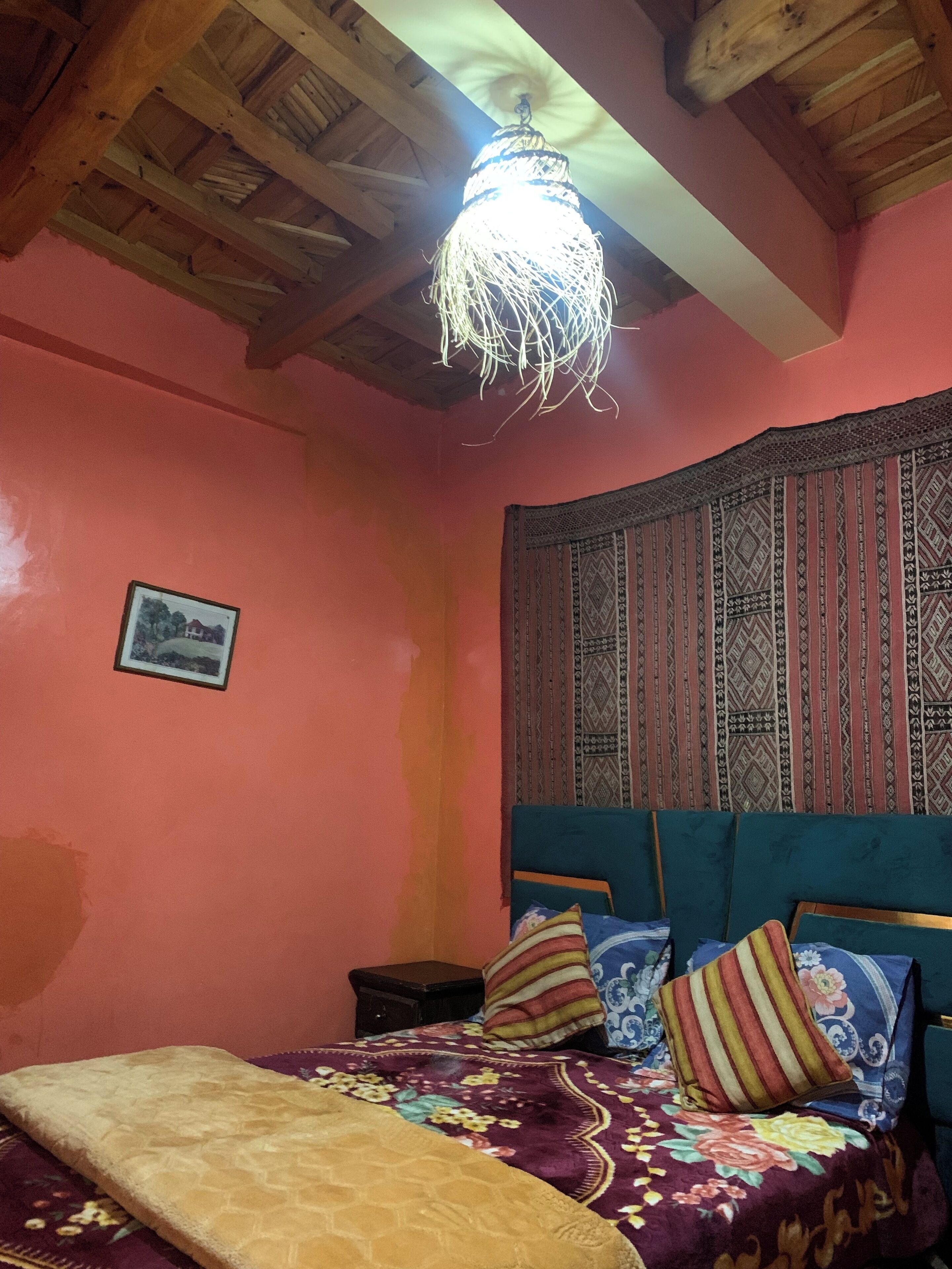 Un dormitorio con techo de madera, cabecera estampada, cama con ropa de cama floral y un cuadro en la pared.