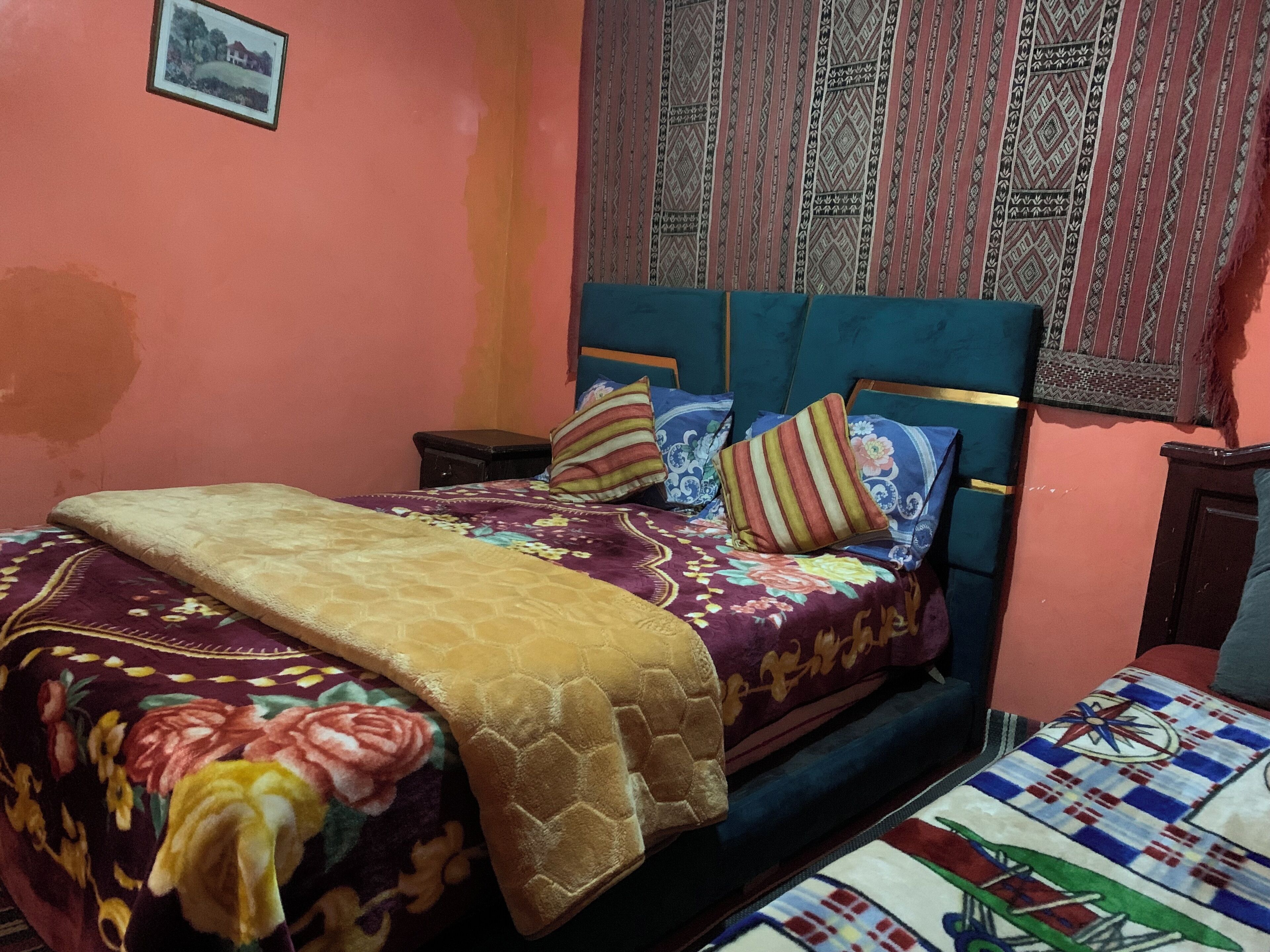 A bedroom with a bed, pillows, a blanket, a nightstand, and a wall-mounted picture.