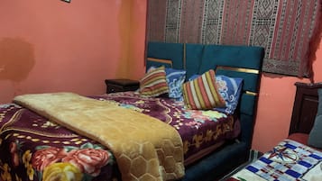 A bedroom with a bed, pillows, a blanket, a nightstand, and a wall-mounted picture.