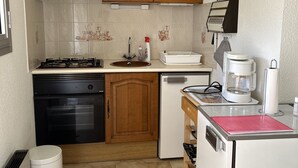 Une cuisine de taille réduite, avec des meubles en bois, une cuisinière noire, un réfrigérateur blanc et une machine à café.