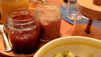 Una mesa de madera con un tazón de kiwi en rodajas, una cuchara y varios frascos de vidrio con distintos alimentos.