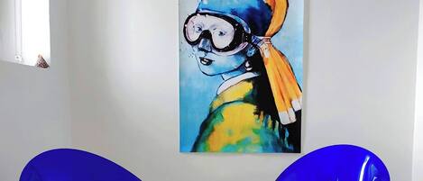Dos sillas azules con una mesa de vidrio en el medio, un cuadro en la pared y una ventana con vistas.