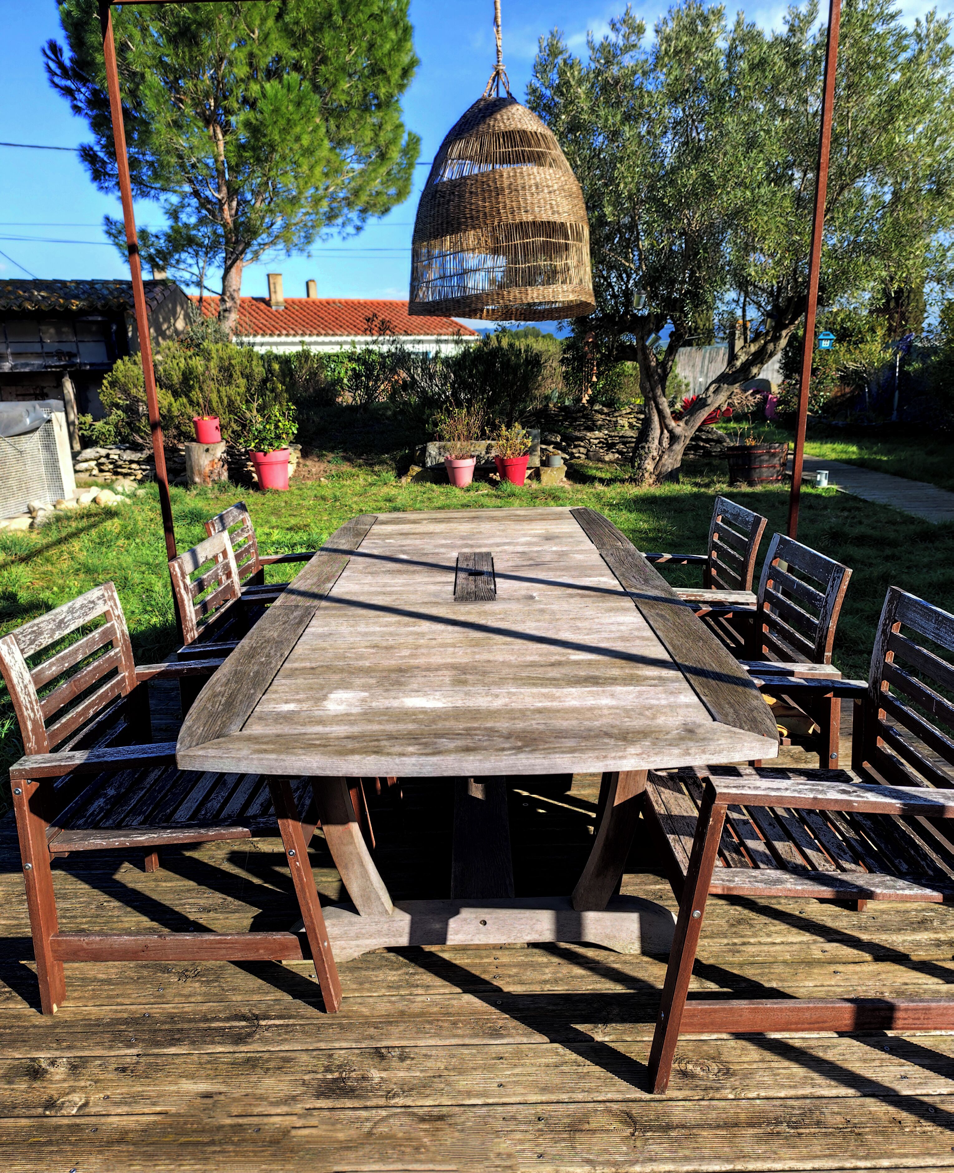 A wooden deck with a table and chairs, surrounded by potted plants and trees.