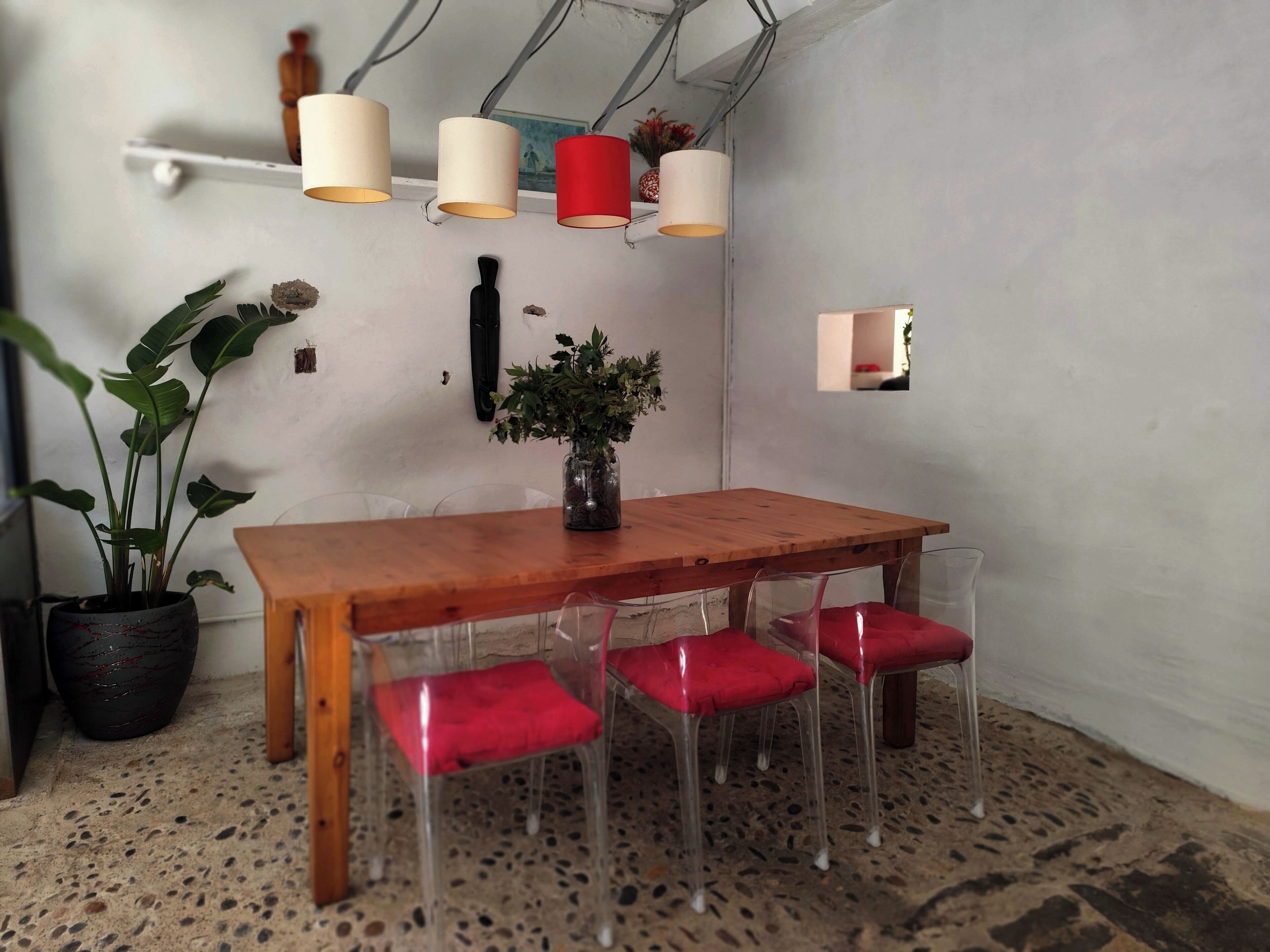 Una mesa de madera con cuatro sillas transparentes, una planta en maceta y un florero con flores sobre la mesa.
