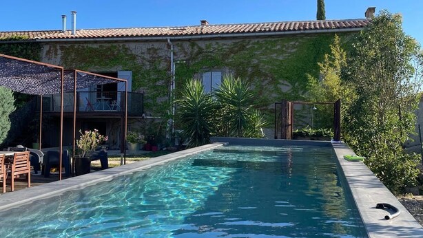 Une piscine à l’eau claire, entourée d’une terrasse aménagée avec des chaises et une table.