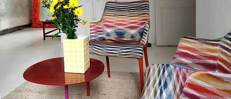Una sala de estar con una mesa roja, un sillón colorido y un sofá estampado.