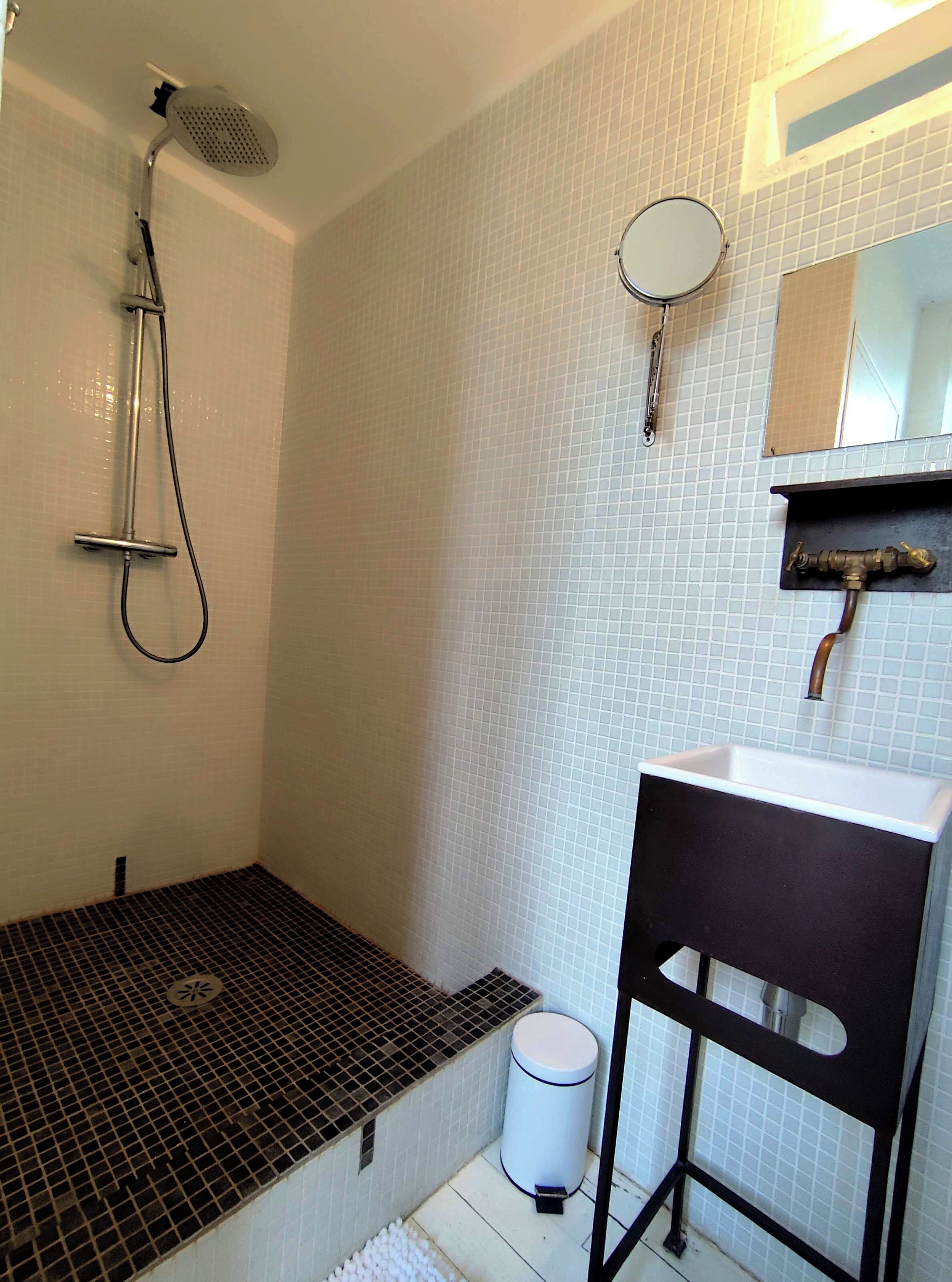 A bathroom with a shower, sink, mirror, and tiled walls.