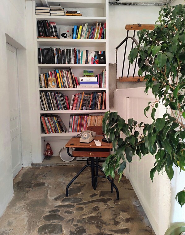 A corner with a bookshelf filled with books, a wooden desk with a telephone and a small figurine, and a potted plant. - Les Grands Cyprès - chambres d'hôtes, bed and breakfast (Conques-sur-Orbiel)