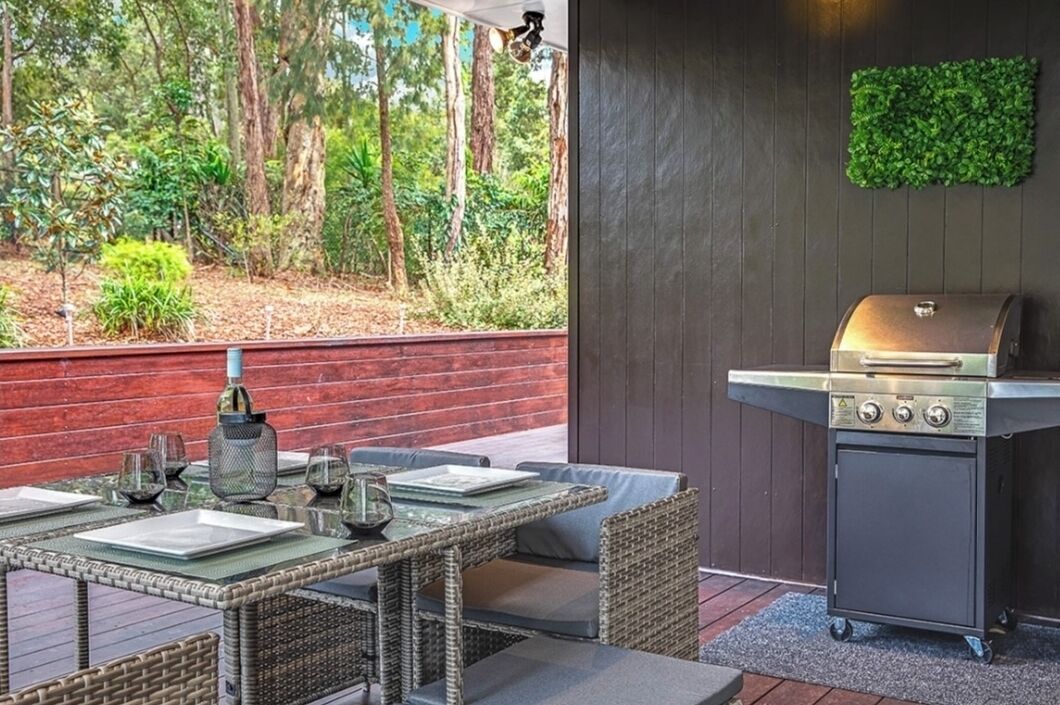 An outdoor patio with a grill, wicker furniture, and a view of a forest.
