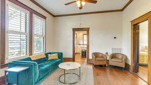 A spacious living room with a teal sofa, a round coffee table, and two armchairs. A ceiling fan and a window with blinds are visible. - Walkable & Historic Houston Heights Bungalow! (Houston)