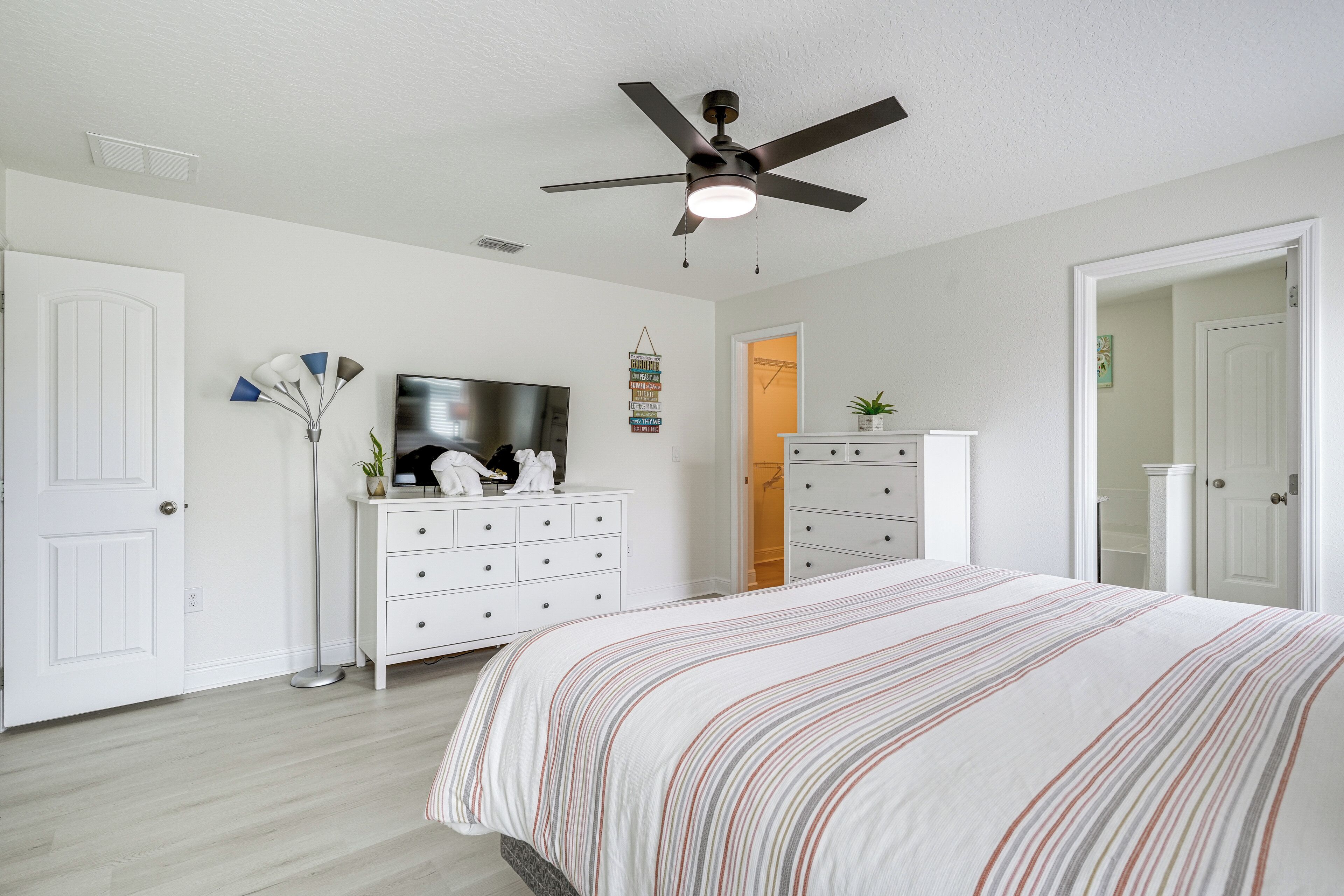 A bedroom with a bed, a ceiling fan, a dresser, and a television.