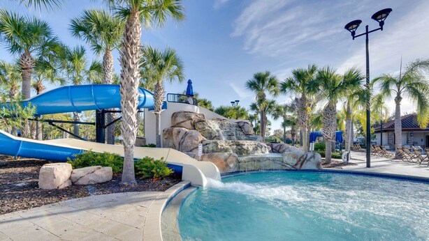 A pool with a water slide, palm trees, and a rock waterfall.