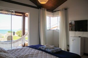 Un dormitorio con cama, televisor, refrigerador y una hamaca junto a una ventana grande con vistas.