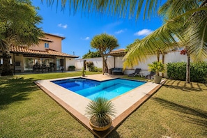 A swimming pool with a tiled deck, surrounded by grass and palm trees. - Bz04 30 passos da praia casa piscina (Buzios)
