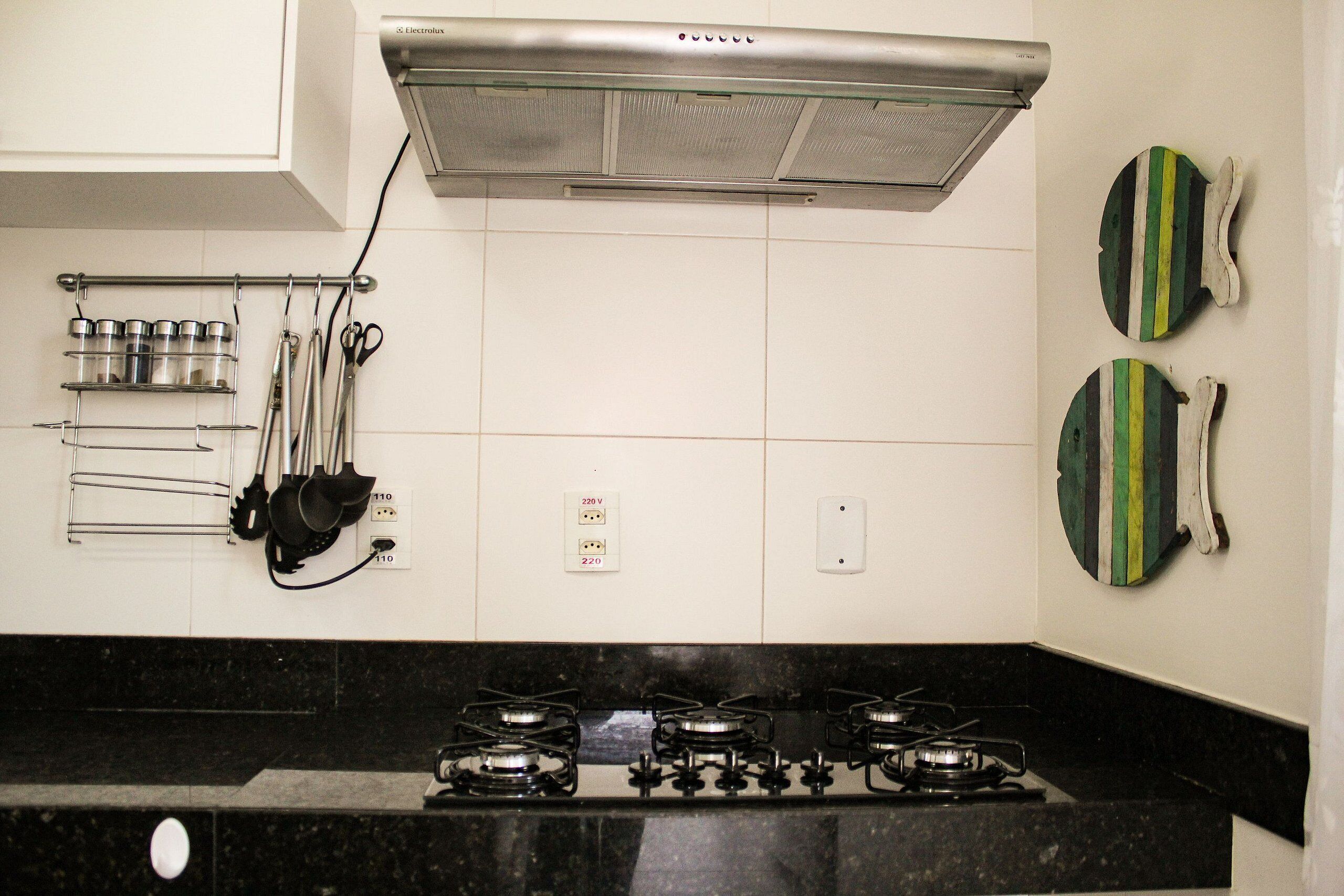 A kitchen with a gas stove, a stainless steel range hood, and a wall-mounted utensil rack.