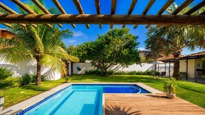 Una piscina con cubierta de madera, rodeada de palmeras y un muro blanco.
