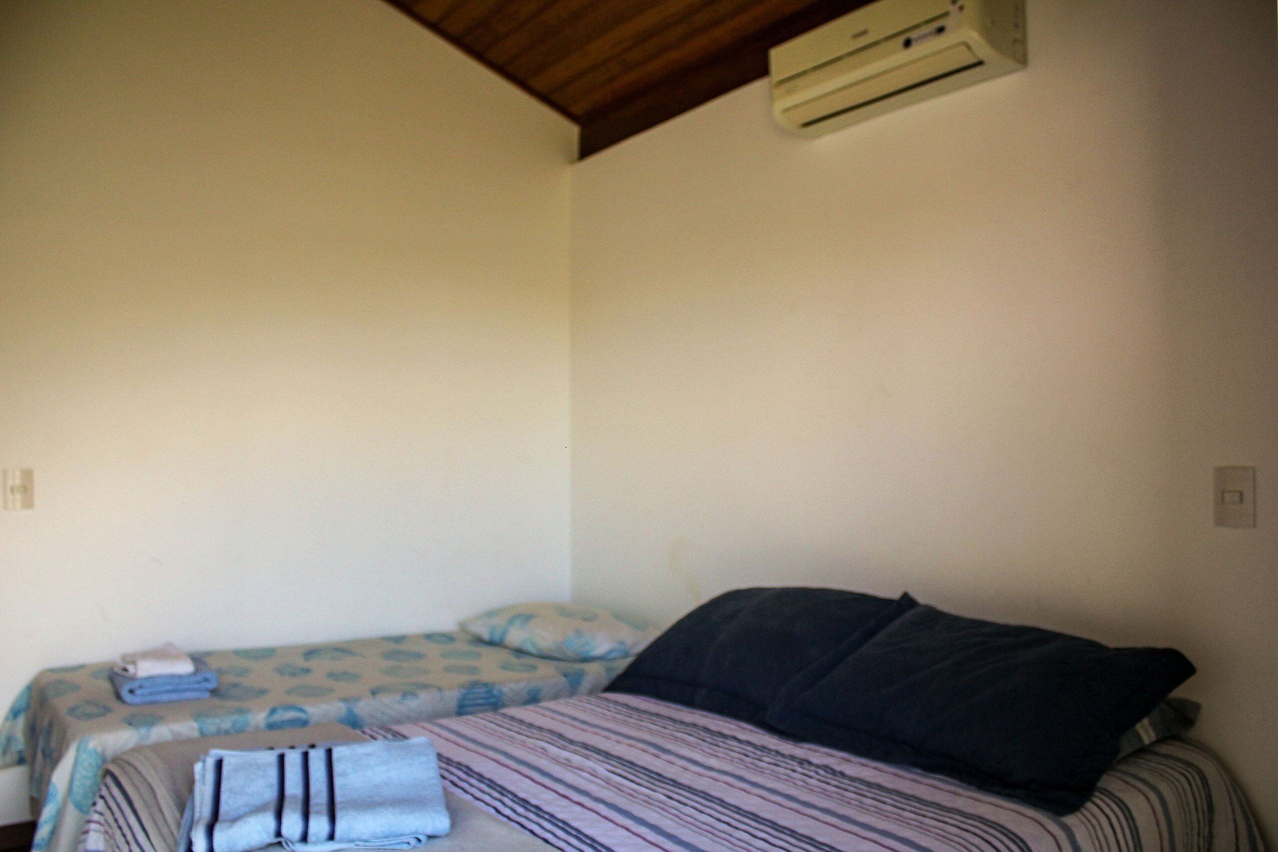 Una habitación con dos camas, una con una colcha a rayas y la otra con una colcha azul estampada de flores. Hay un aire acondicionado instalado en la pared sobre las camas.
