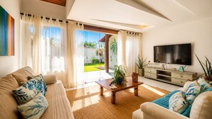 Una sala de estar moderna con sofá, mesa de centro, televisor y vistas a un jardín.