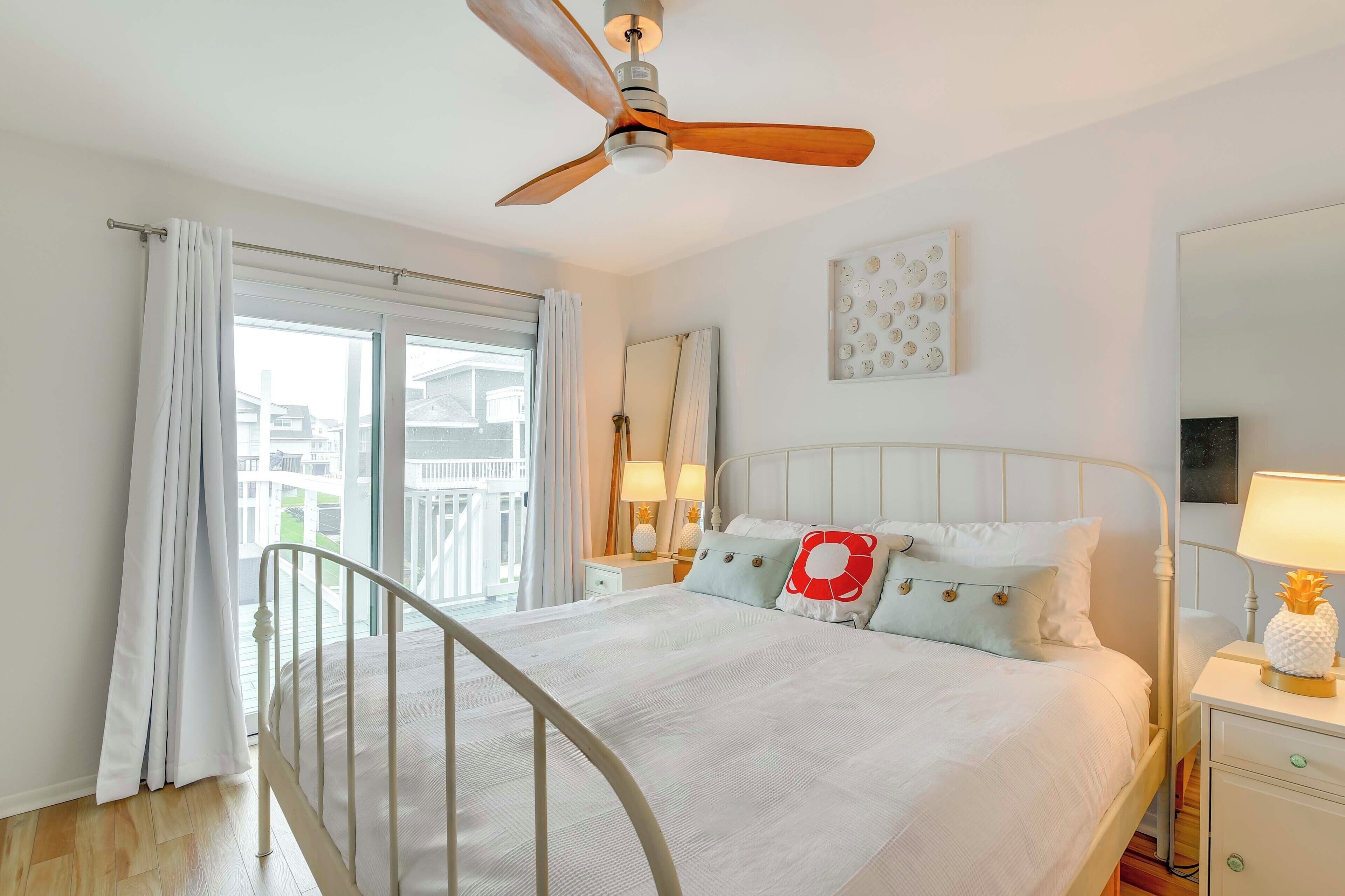 A bedroom with a bed, a ceiling fan, a nightstand, a lamp, and a window with curtains.