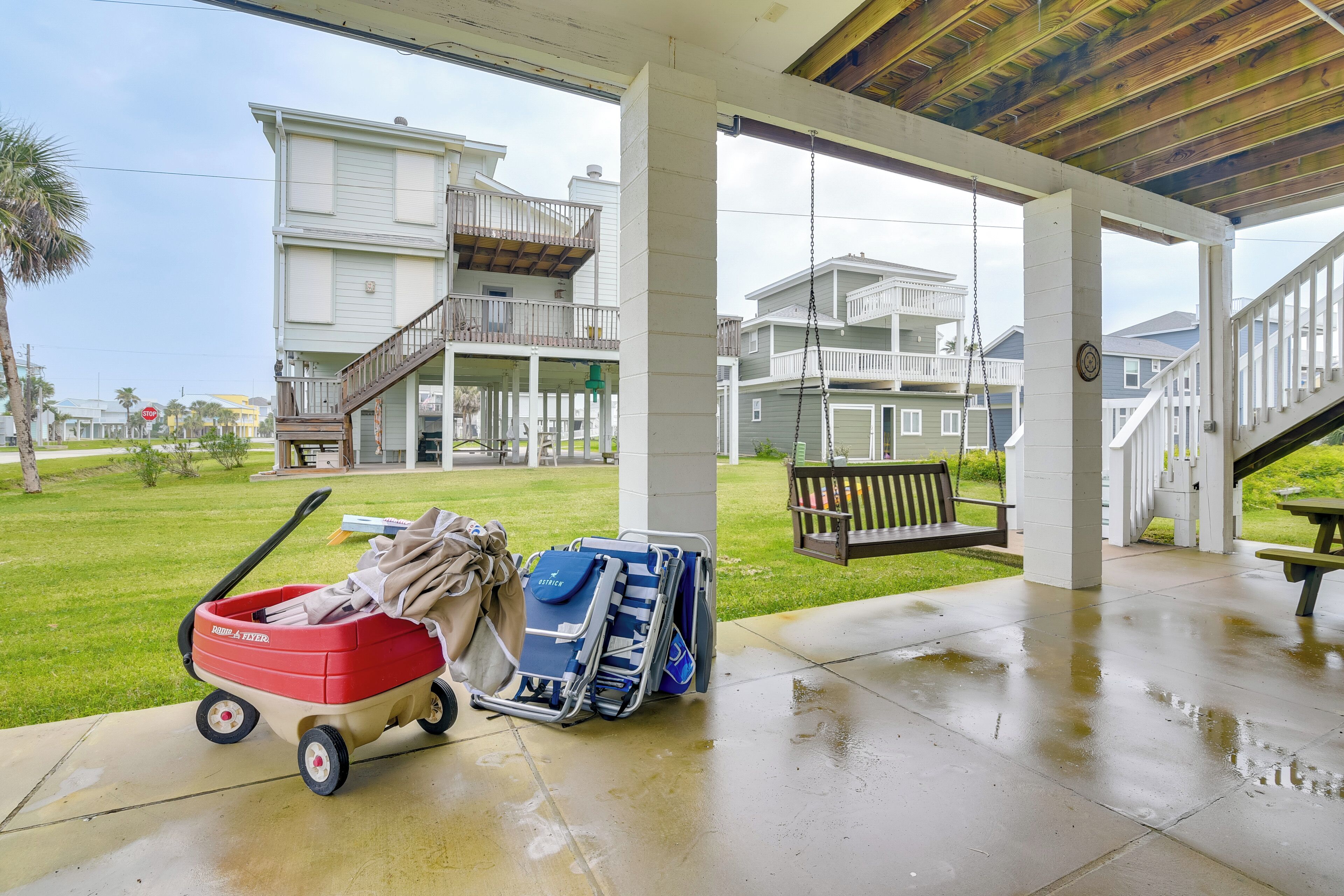 A covered outdoor area with a concrete floor, a red and beige wagon, and stacked chairs.