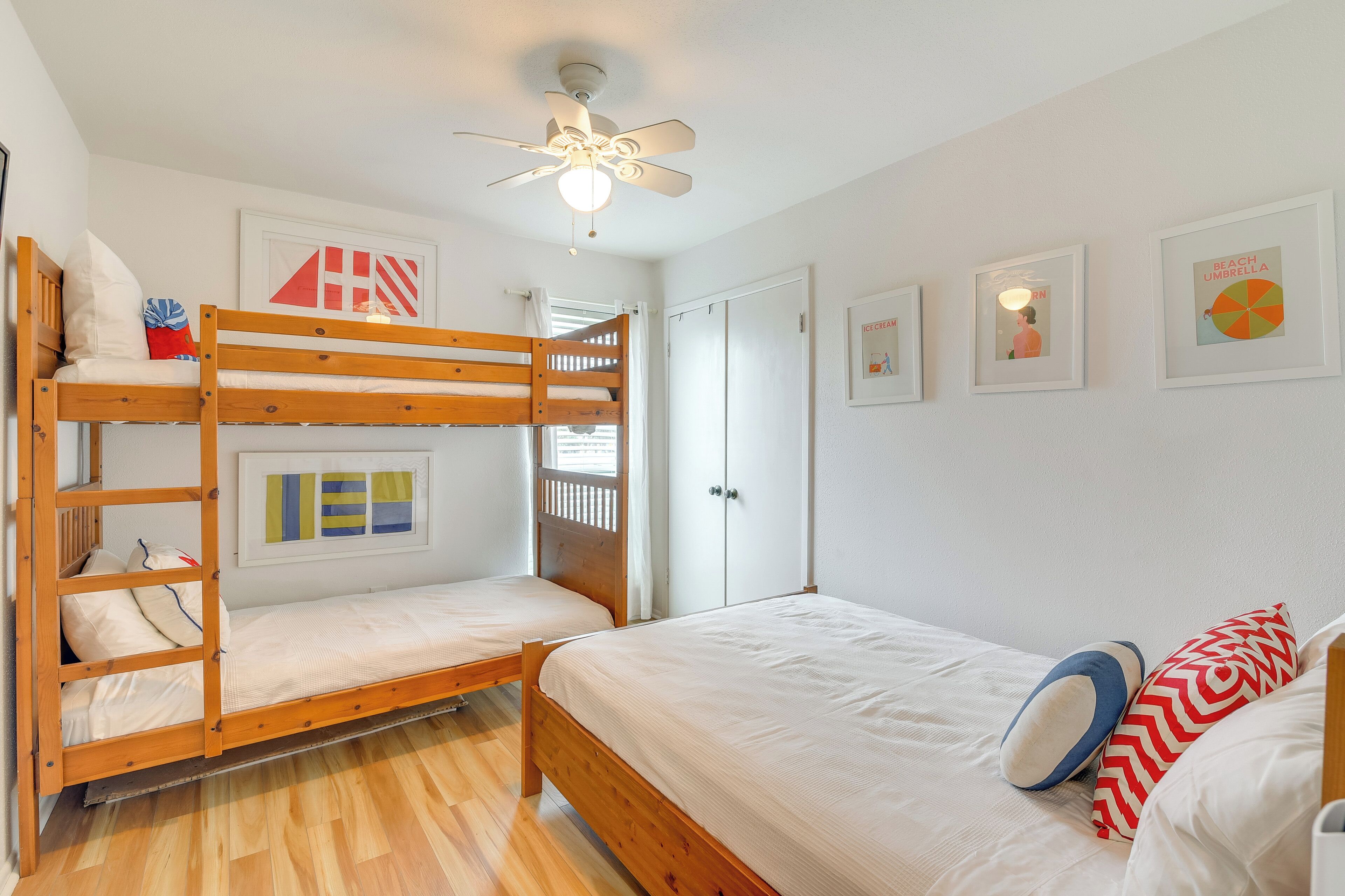 Een slaapkamer met stapelbed, plafondventilator, witte muren en kunstwerken in lijsten.