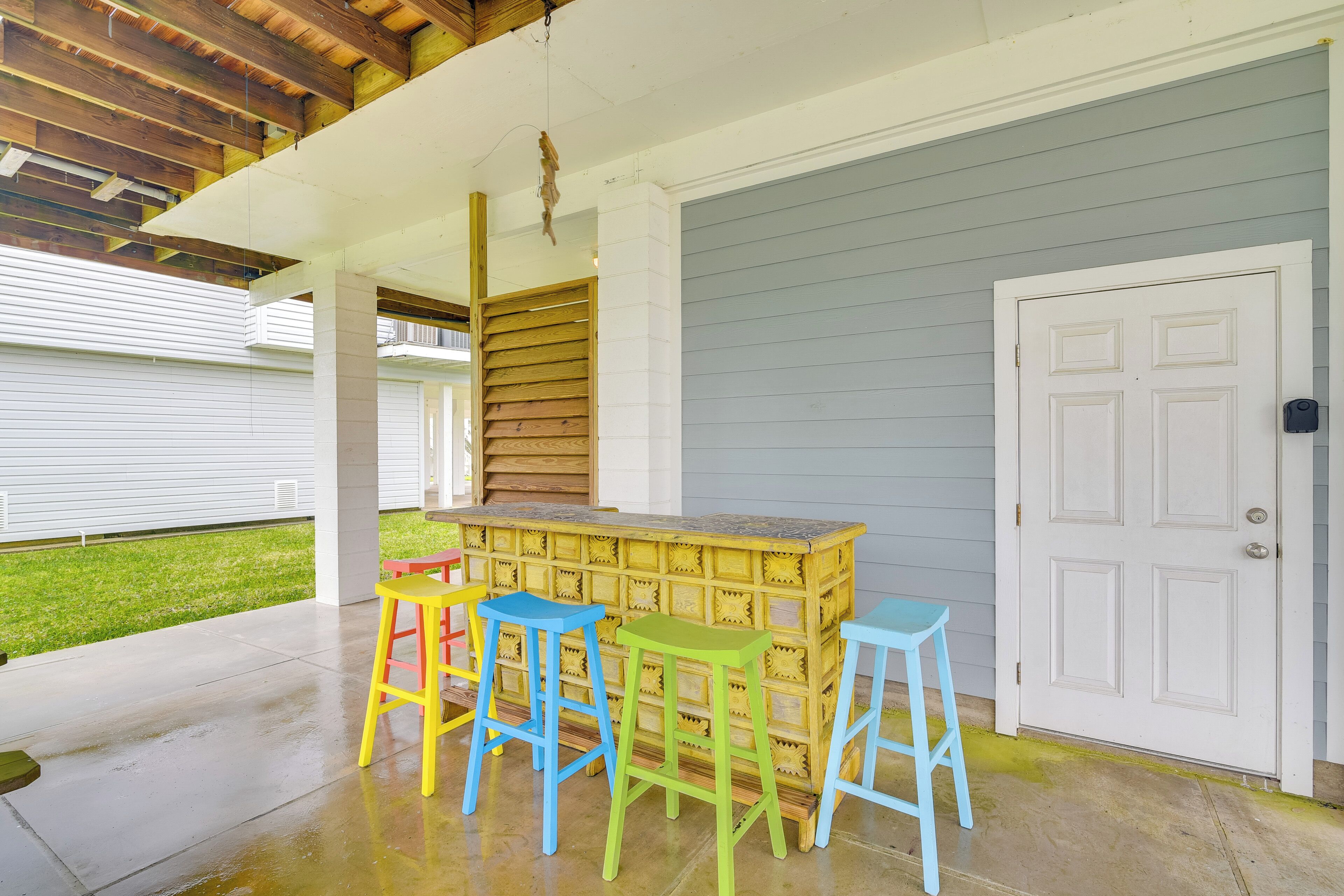 An outdoor patio area with a wooden ceiling, a bar counter, and colorful bar stools.