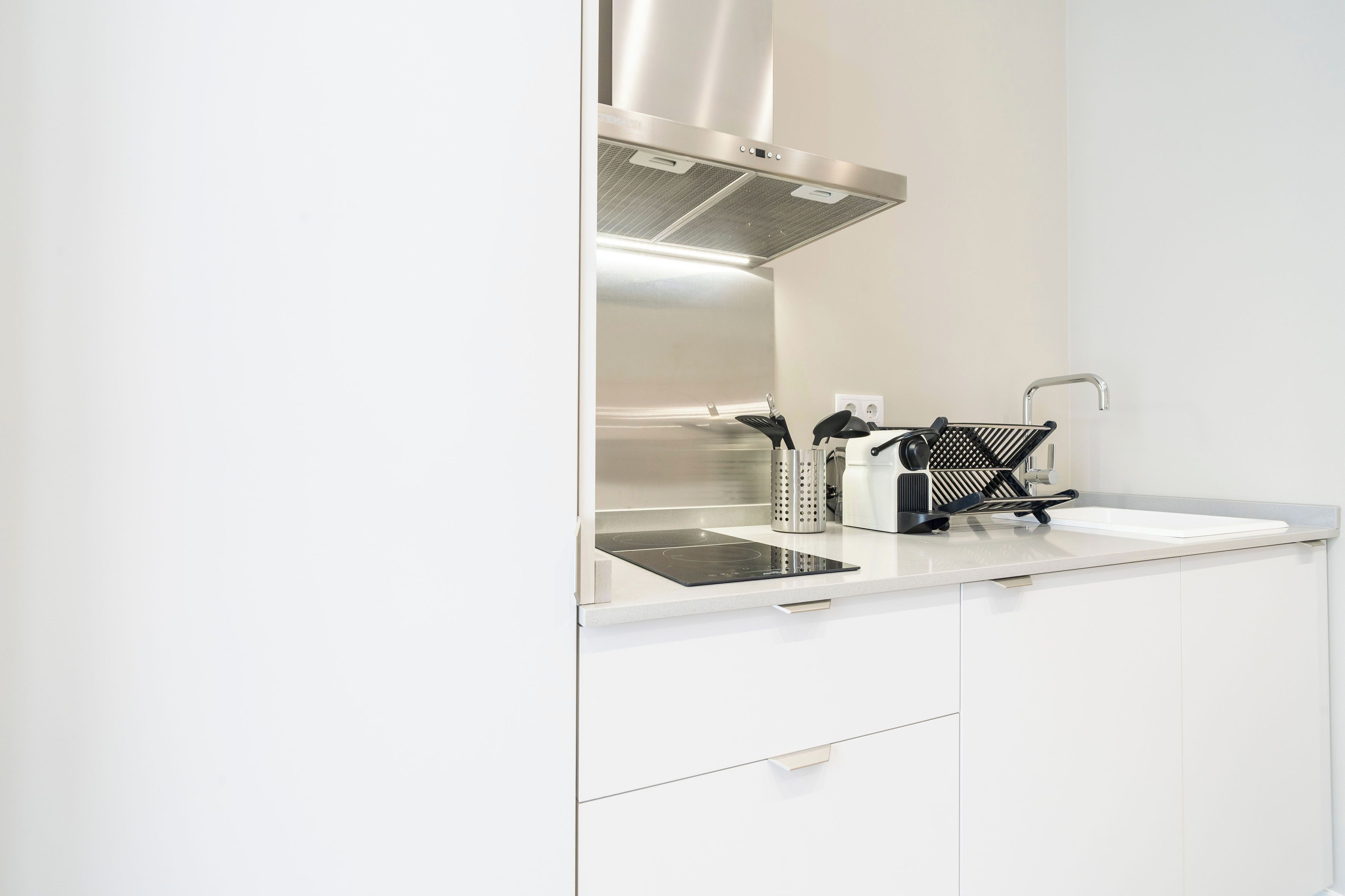 Ett modernt kök med vita skåp, en köksfläkt i rostfritt stål, en svart induktionshäll och en kaffemaskin.