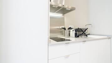 Ett modernt kök med vita skåp, en köksfläkt i rostfritt stål, en svart induktionshäll och en kaffemaskin.