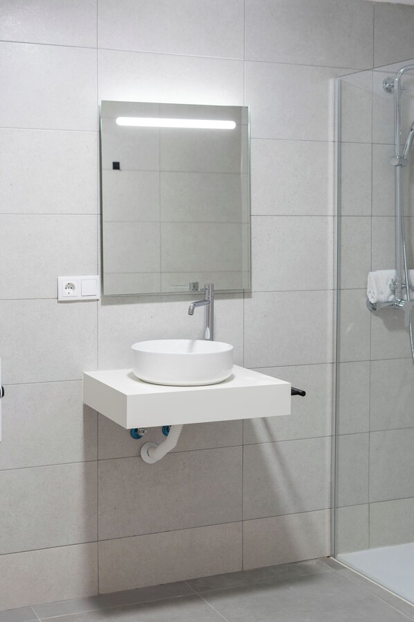 A modern bathroom with a white sink, a mirror, and a glass shower enclosure.