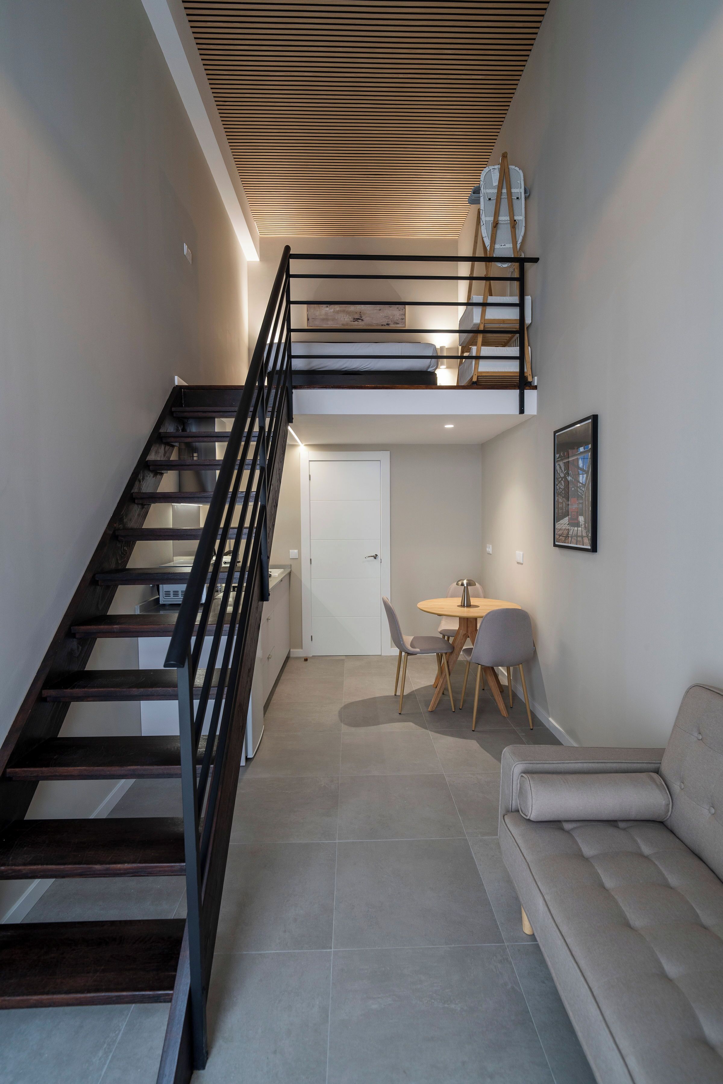 Un interior moderno con una escalera, un sofá, una mesa de comedor y un techo de listones de madera.