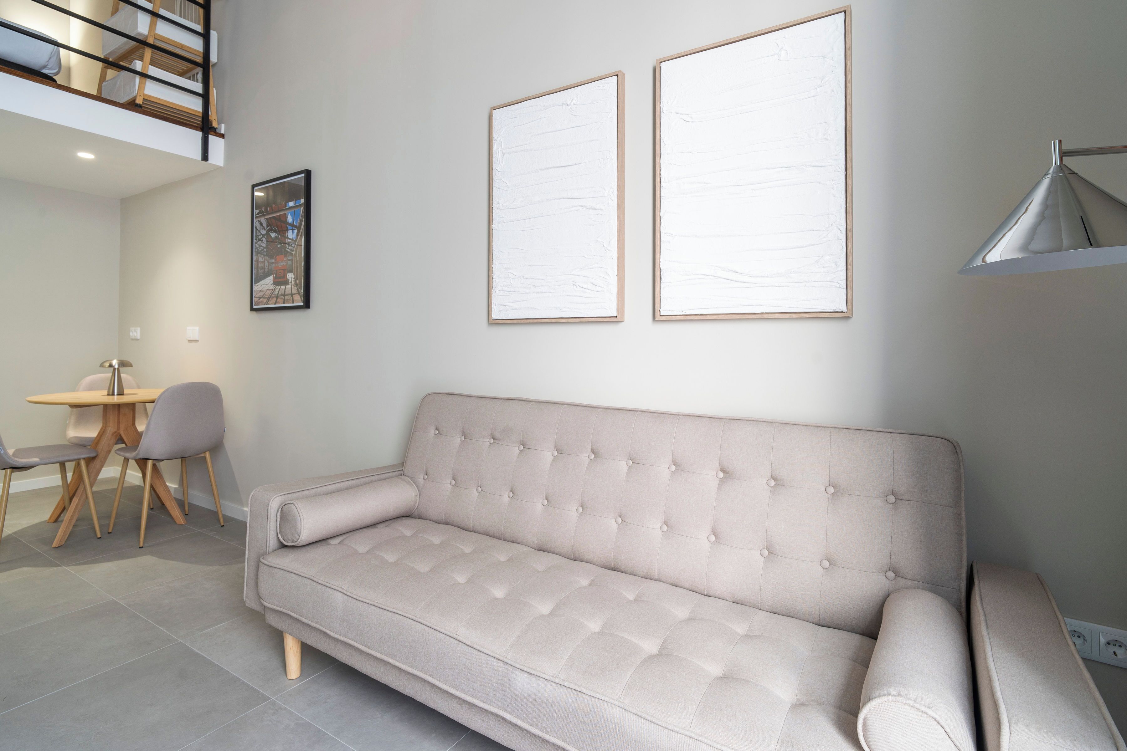 A modern living room with a beige sofa, a dining table with chairs, and two framed artworks on the wall.