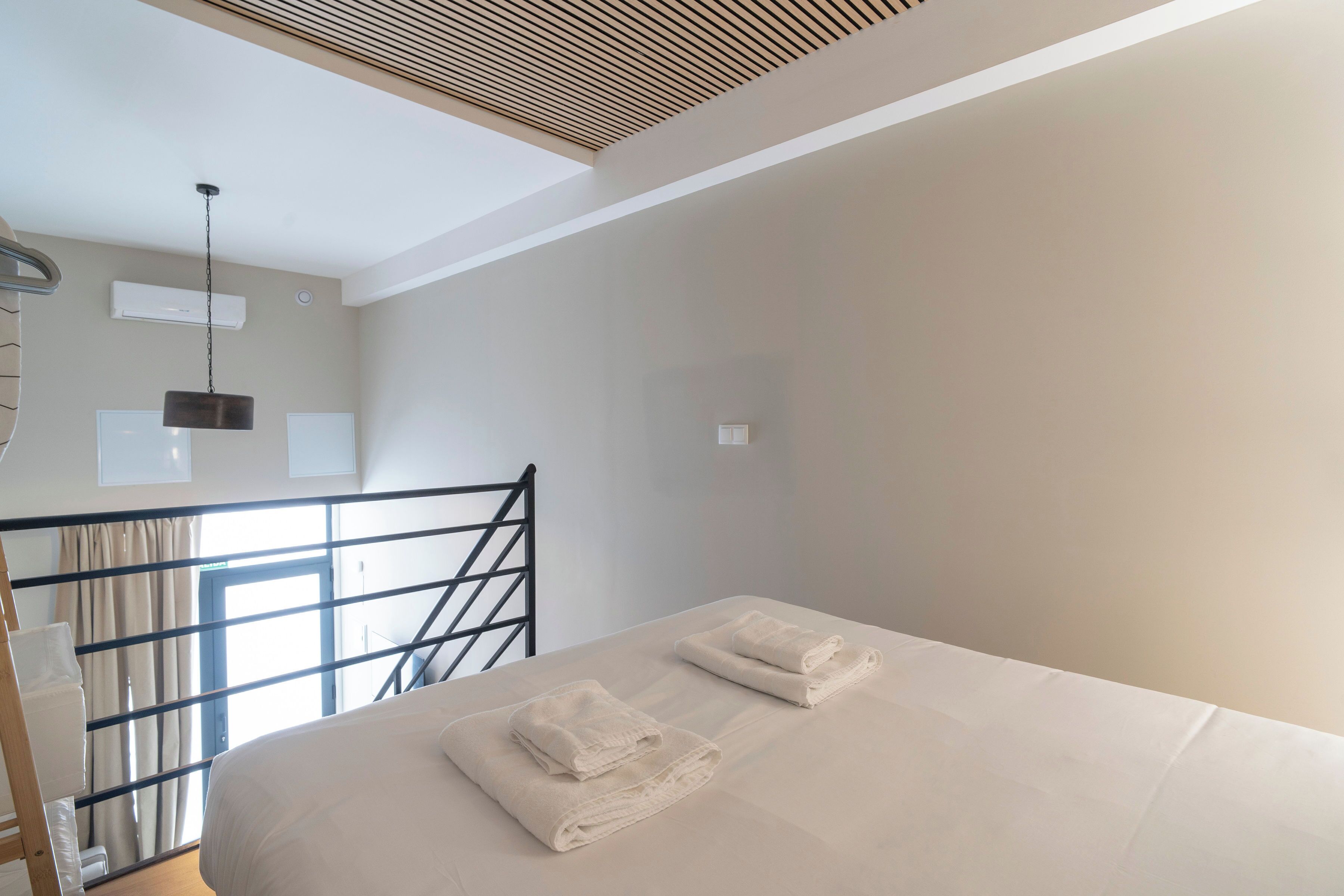Un dormitorio con una cama, dos toallas, una lámpara colgante, una ventana con cortinas y un respiradero en el techo.