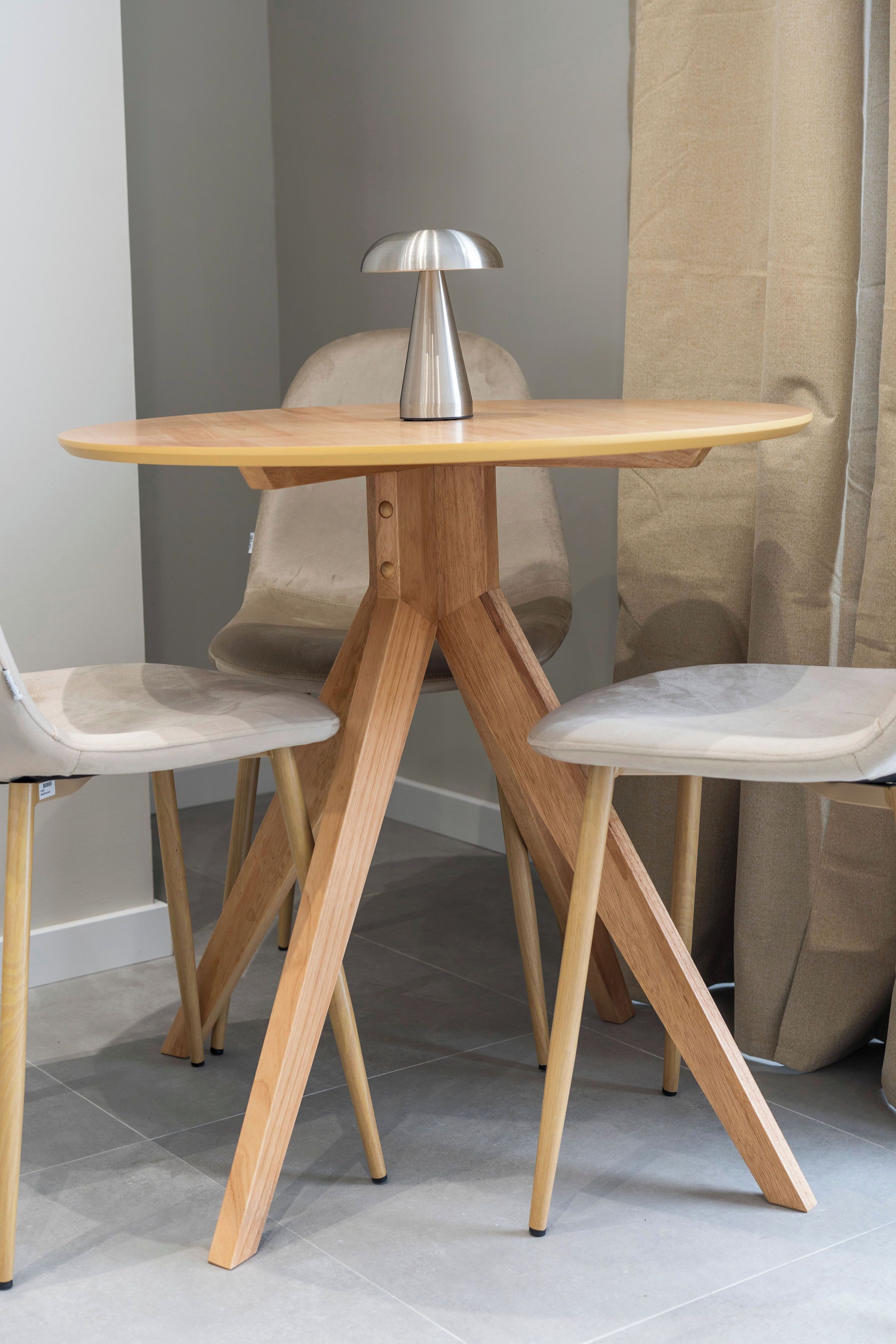 Una mesa redonda de madera con una lámpara de metal, dos sillas y una cortina al fondo.