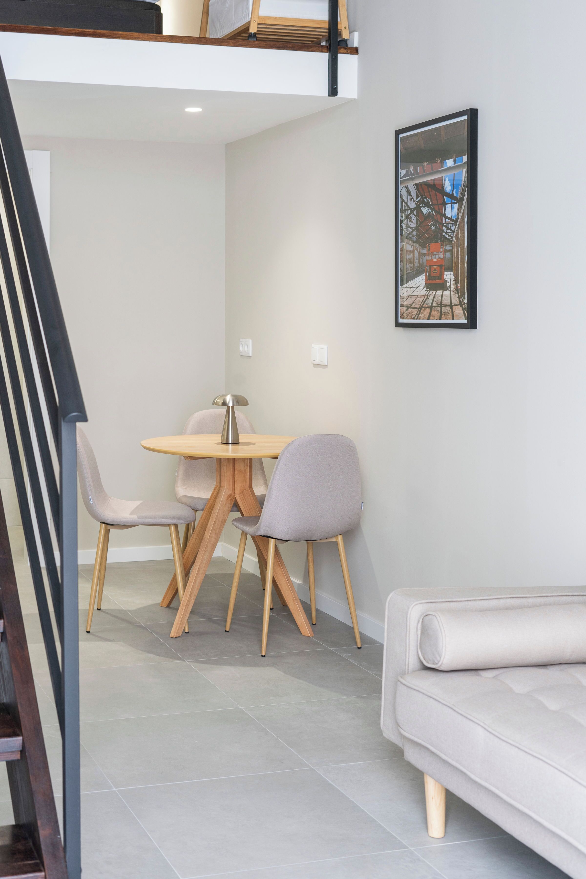 Un comedor moderno con una mesa redonda y cuatro sillas, un sofá y un cuadro en la pared.
