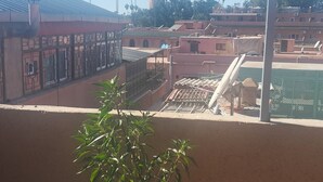 A balcony with a potted plant, a view of a building with a tower, and a clear blue sky. - Hôtel de la paix (Marrakech)