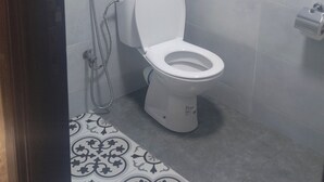 A bathroom with a toilet, a shower, and a patterned floor. - Hôtel de la paix (Marrakech)
