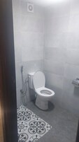Casa de banho com sanita, chuveiro e pavimento estampado.