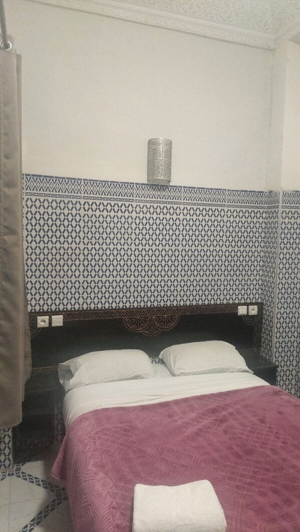 Un lit avec une tête de lit décorée, une table de chevet et un luminaire fixé au mur.