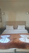 Quarto de hotel com uma cama grande, duas almofadas, um cobertor castanho e duas luminárias laterais.