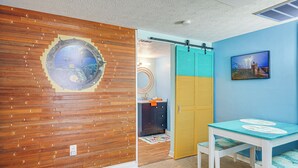 Een kamer met een houten wand, een blauwe wand met een afbeelding, een tafel met een placemat en een deur met een handdoek eraan.