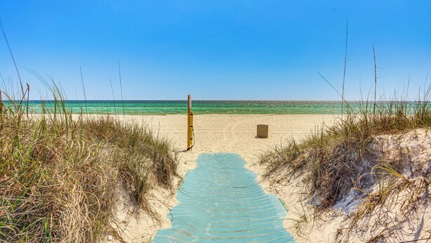 Een strandpad dat naar de oceaan leidt, met duinen en een houten paal.